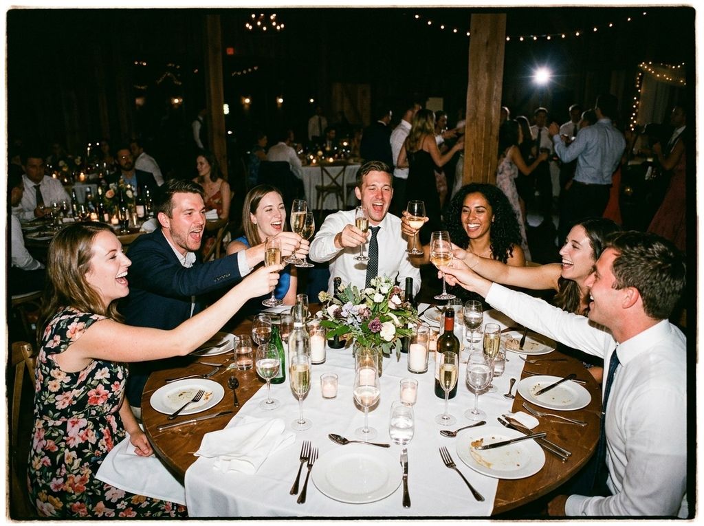 Wedding guests laughing mid-toast at a reception table